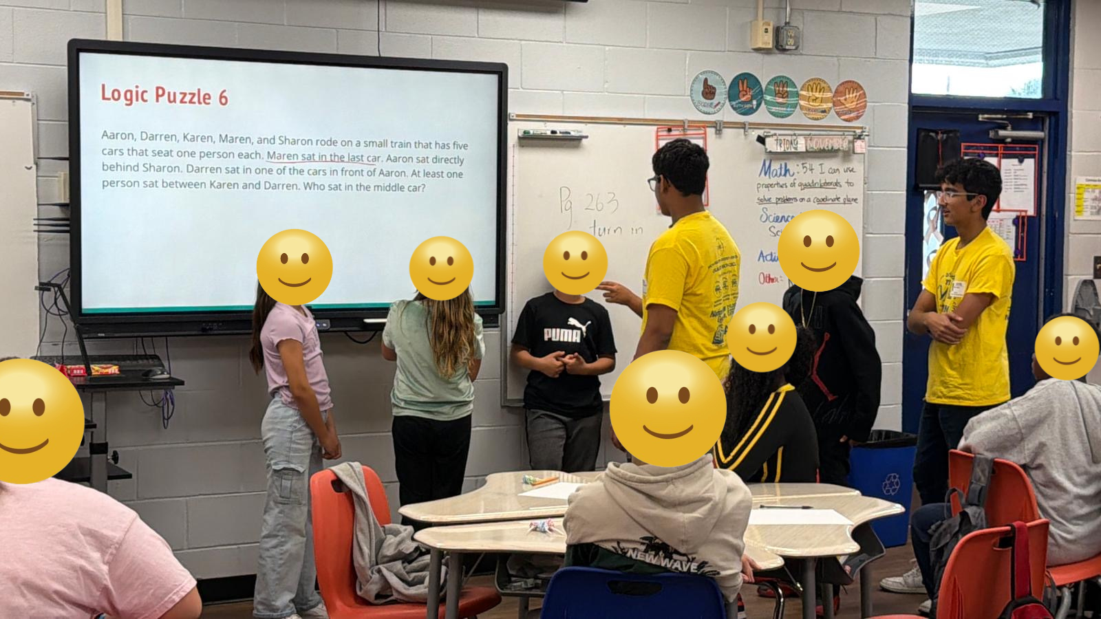 Student volunteers discussing a logic puzzle at University Park Elementary, with pupils’ faces covered in the original photo
